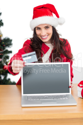 Festive brunette showing credit card and screen of laptop
