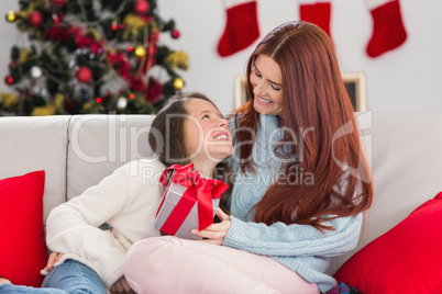 Festive mother and daughter on the couch with gift