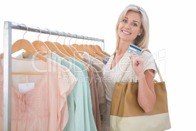 Pretty blonde smiling at camera by clothes rail