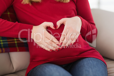 Close up of a pregnant woman doing heart sign on her belly