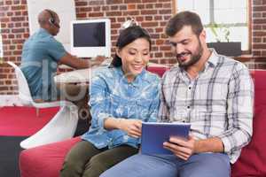 Casual colleagues using digital tablet on couch