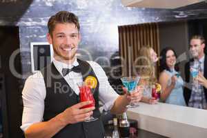 Handsome barman smiling at camera holding cocktails
