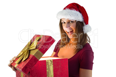 Pretty brunette in santa hat opening a gift smiling at camera