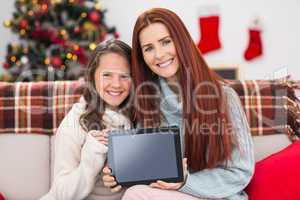 Festive mother and daughter showing tablet on the couch