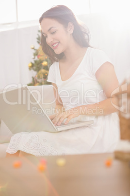 Smiling brunette typing on her laptop on the couch