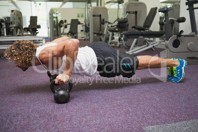 Young man doing push ups with kettle bells in gym