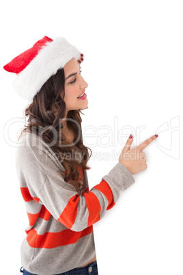 Smiling brunette in santa hat pointing white poster