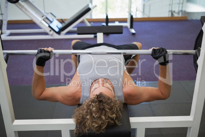 Young muscular man lifting barbell in gym