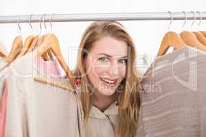 Pretty blonde smiling at camera by clothes rail