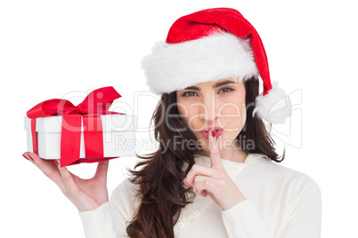 Festive brunette holding gift and keeping a secret