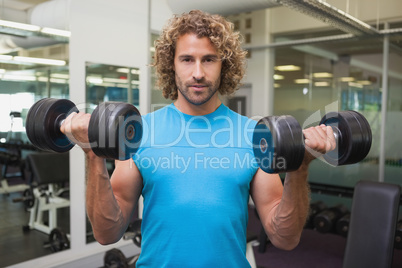 Handsome young man exercising with dumbbells in gym