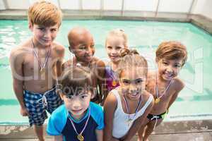 Cute swimming class smiling poolside with medals