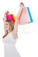 Happy blonde holding up shopping bags in white dress