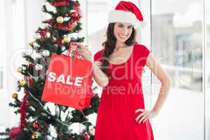 Stylish brunette in red dress showing sale bag at christmas
