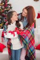 Festive mother and daughter wrapped in blanket with gifts