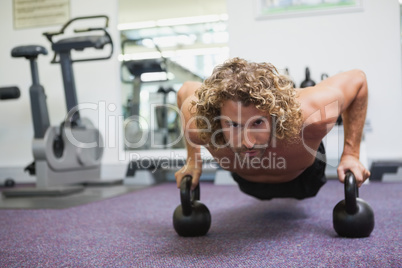 Handsome man doing push ups with kettle bells in gym