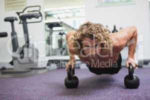 Handsome man doing push ups with kettle bells in gym