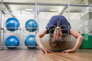 Handsome man stretching on fitness ball in gym