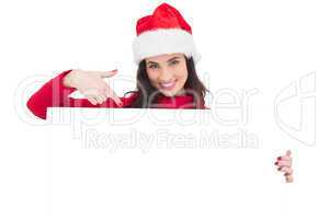 Pretty brunette in santa hat pointing white poster