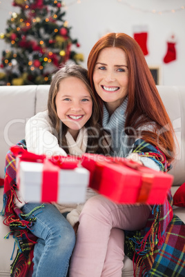 Festive mother and daughter wrapped in blanket with gifts