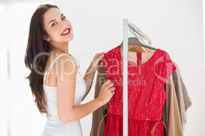 Smiling shopping brunette looking at red dress