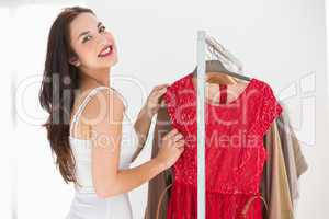 Smiling shopping brunette looking at red dress