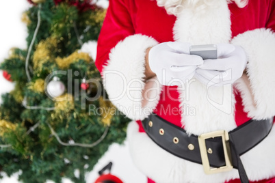 Santa using smartphone with christmas tree behind him