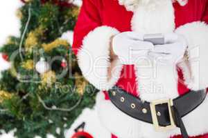 Santa using smartphone with christmas tree behind him