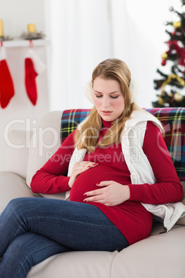 Pregnant woman sitting on couch touching her belly