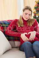 Cute pregnant woman making heart shape on belly