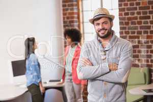 Man with arms crossed and colleagues behind in office