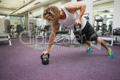 Side view of man exercising with kettle bells in gym