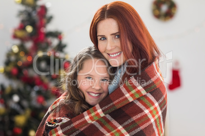 Festive mother and daughter wrapped in blanket