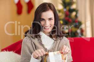 Brunette opening a gift on the couch at christmas