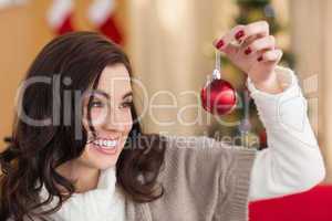 Smiling brunette holding a bauble at christmas