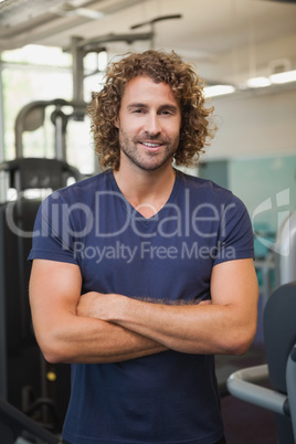 Smiling handsome trainer with arms crossed in gym