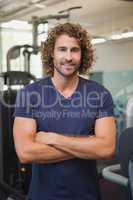 Smiling handsome trainer with arms crossed in gym