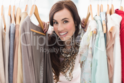 Pretty brunette smiling at camera by clothes rail