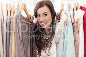 Pretty brunette smiling at camera by clothes rail