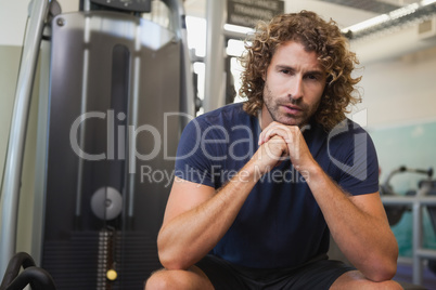 Serious handsome trainer sitting in gym