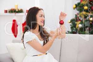 Happy brunette holding a red bauble at christmas