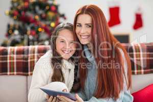 Festive mother and daughter using tablet on the couch