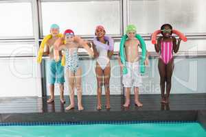 Cute little kids standing poolside with foam rollers