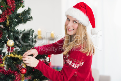 Woman decorating a Christmas tree while looking at camera