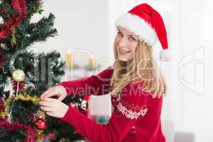 Woman decorating a Christmas tree while looking at camera
