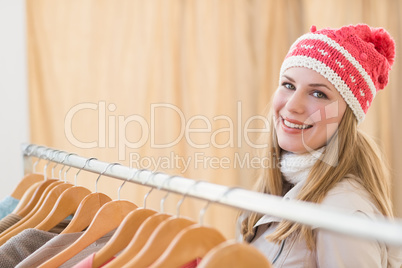 Pretty blonde smiling at camera by clothes rail