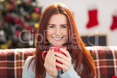 Festive redhead holding mug on couch