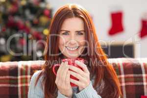 Festive redhead holding mug on couch