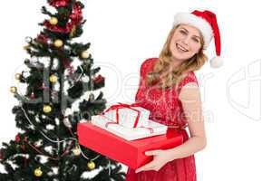 Blonde holding pile of gifts with christmas tree behind her