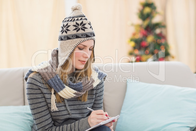 Pretty blonde with winter hat on writing on her notebook